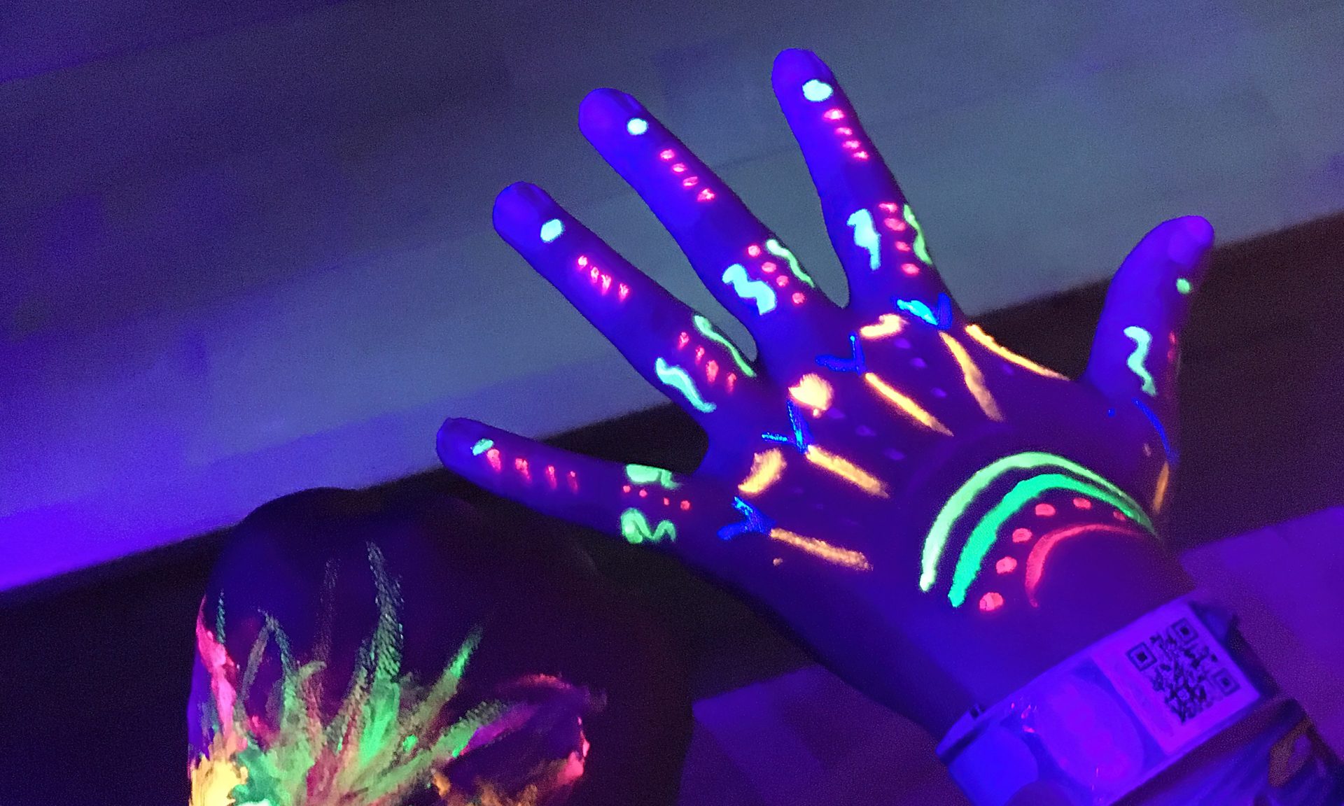 Käsi, jossa ultravioletti-valoon reagoivat maalit hehkuvat värikkäästi