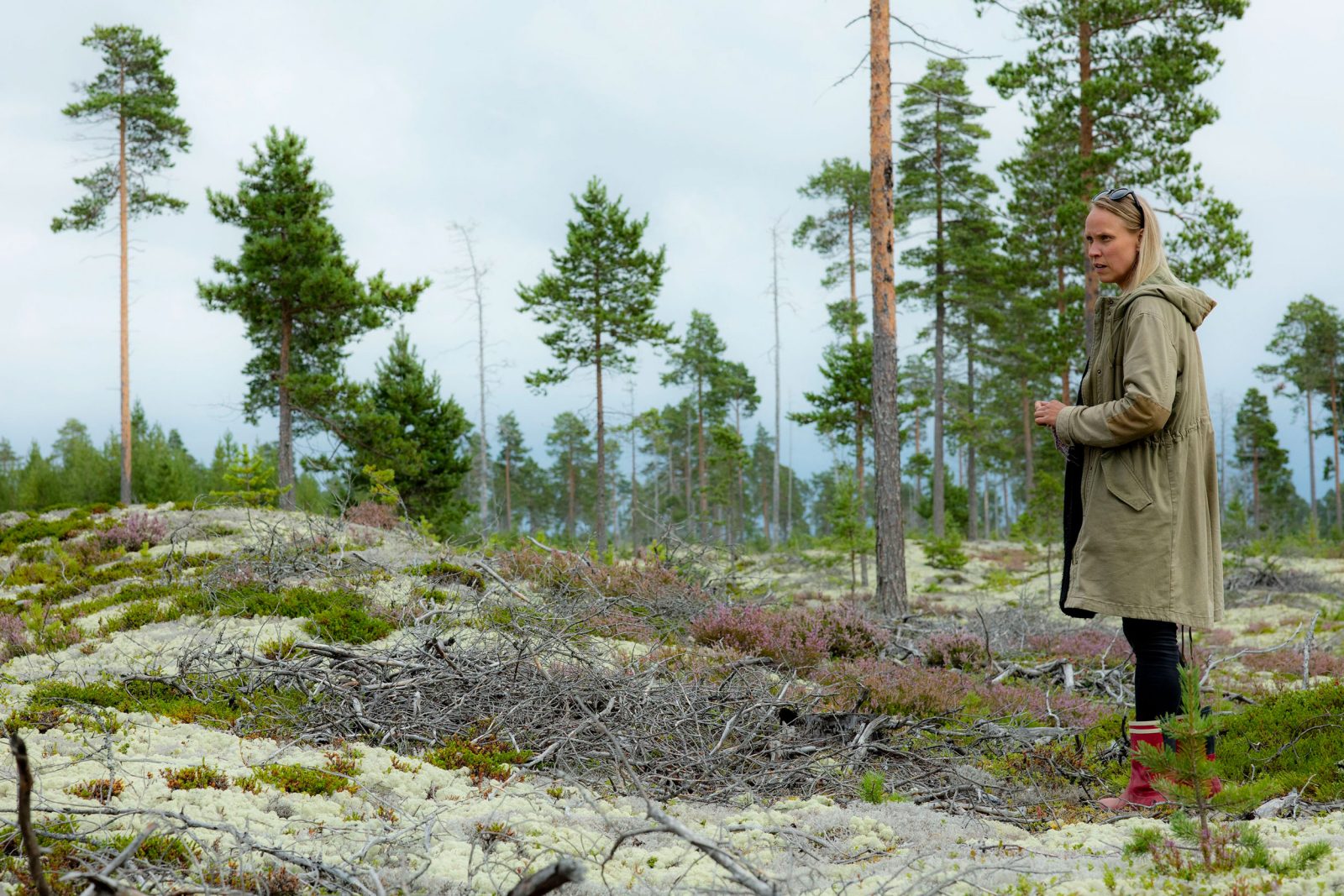 Taiteilija Eija Ranta seisoo kumisaappaat jalassa metsässä, jossa näkyy sammalta ja mäntyjä