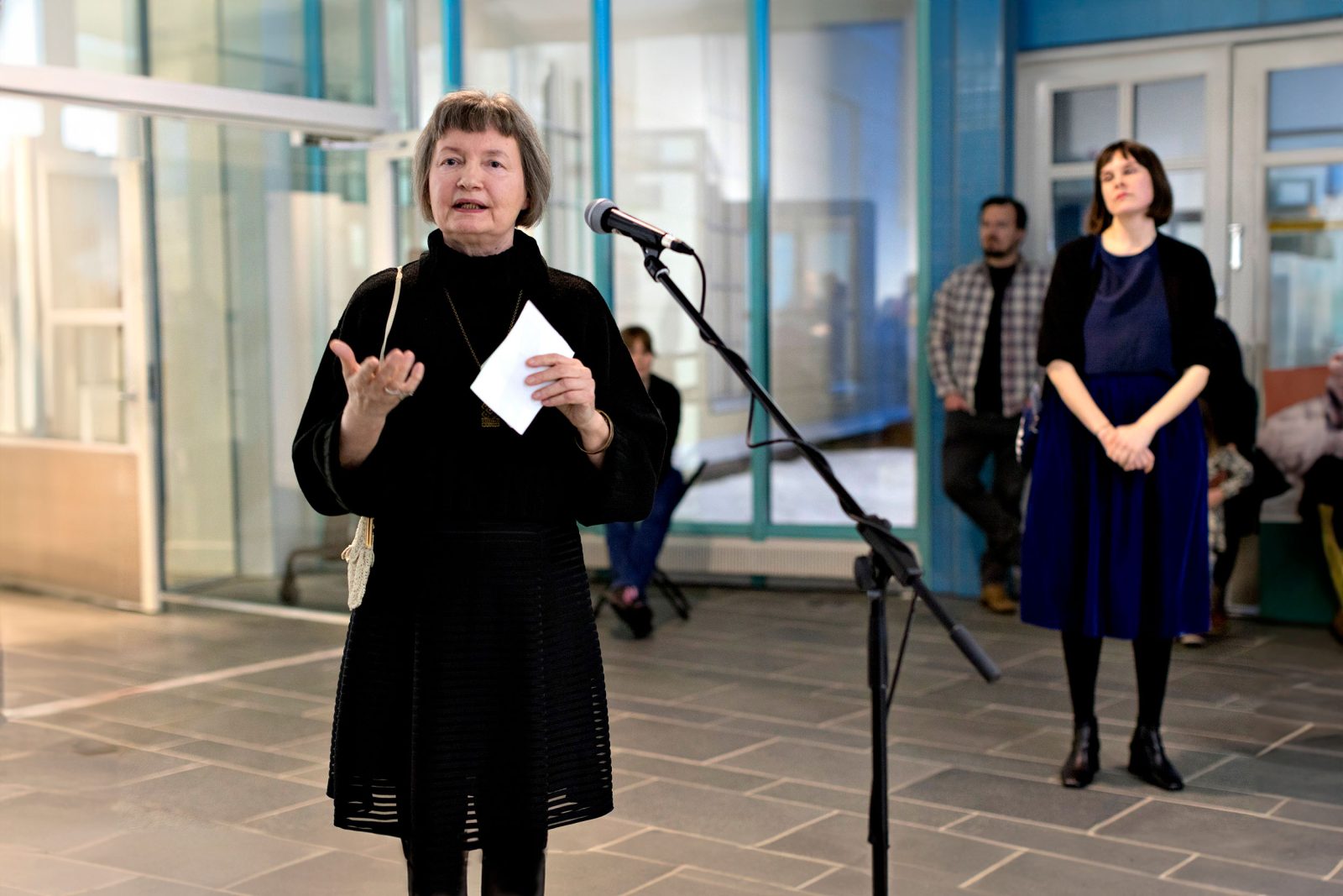Riitta-Alina Helevä pitämässä avajaispuhetta mikrofonin edessä, taidemuseon näyttelysalissa