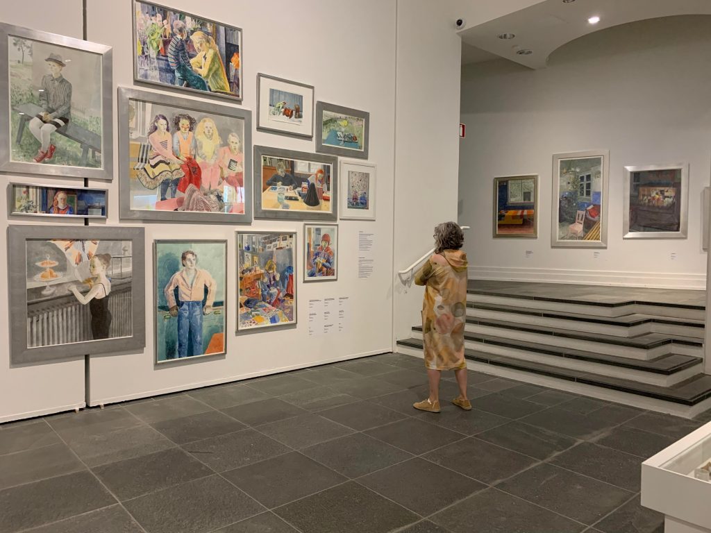 Nainen katselee taideteoksia näyttelysalin seinällä