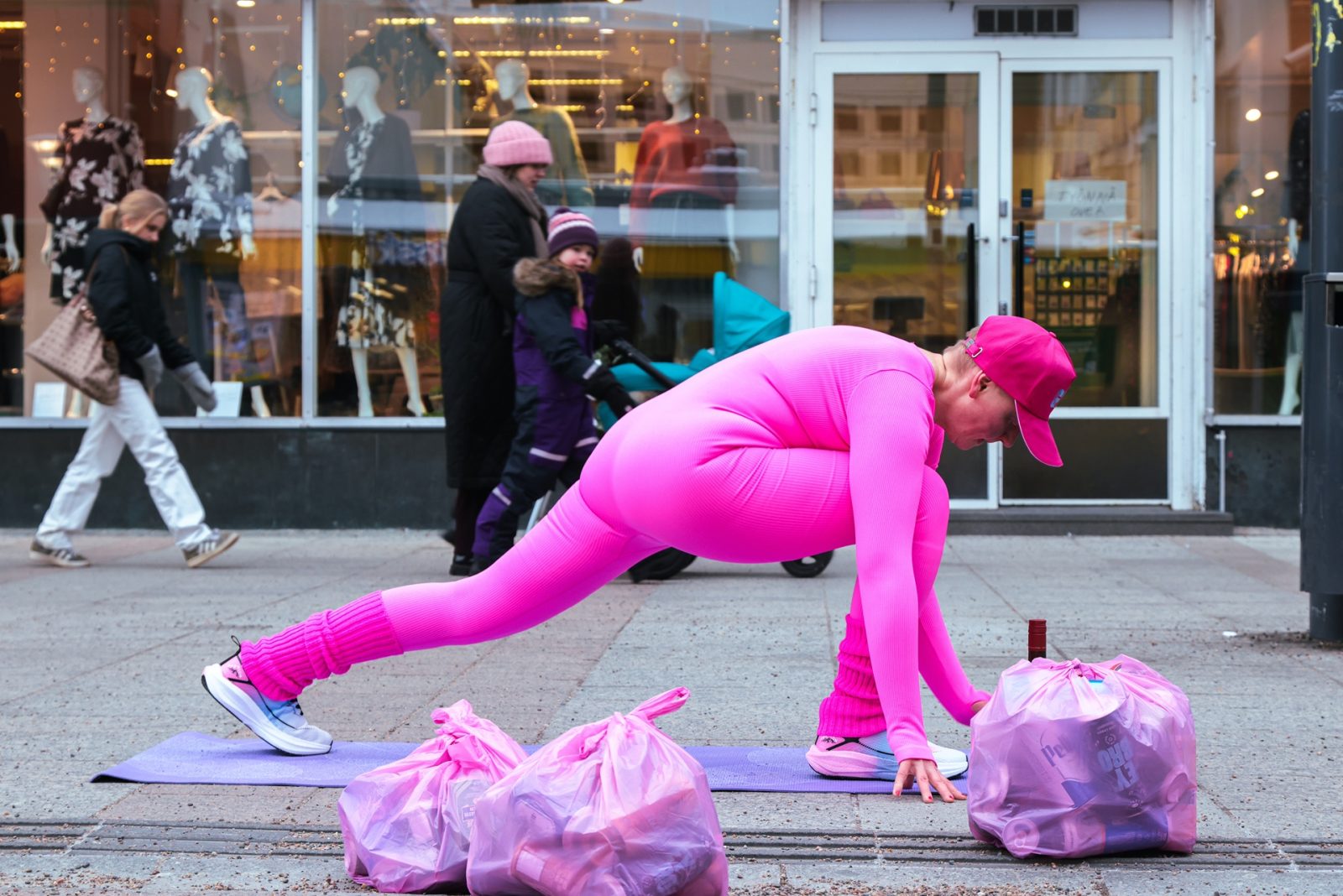Hahmo joogaa kadulla, taustalla kulkee ihmisiä.